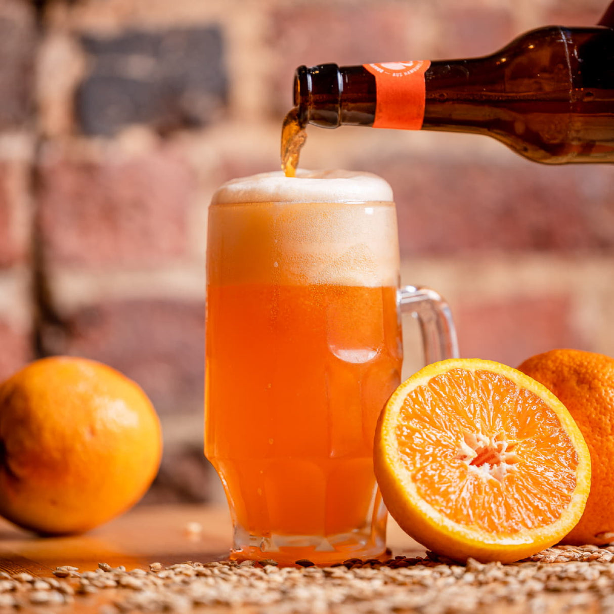 Ein volles Bierglas in dem Gröninger Alster Orange eingefüllt wird. Orangen liegen neben dem Glas