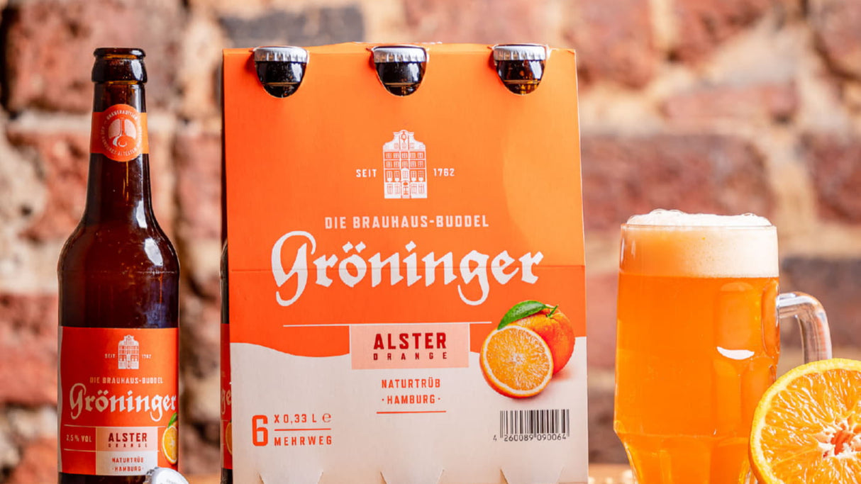 Links eine Flasche Gröninger Alster Orange in der Mitte ein Sechserträger des Bieres und rechts ein Bierkrug aus Glas gefüllt mit dem Getränk